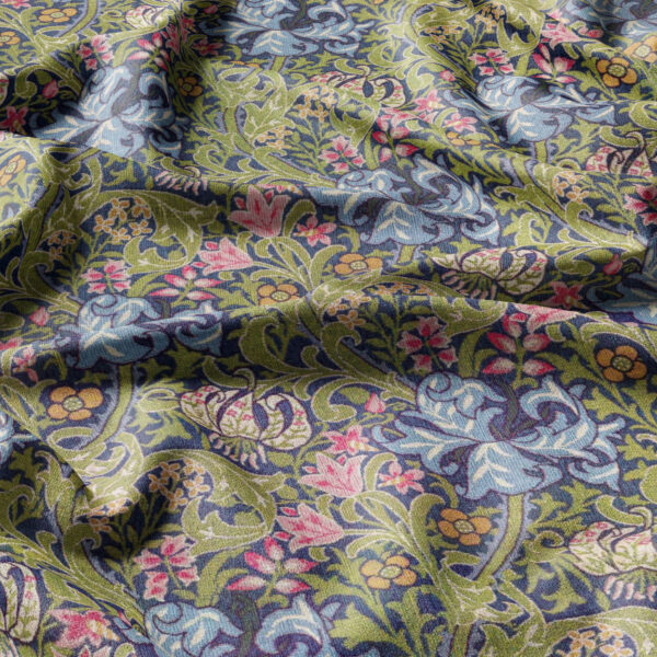 A close-up of William Morris | Pimpernel | Tapestry Fabric shows an intricate floral design with blue, pink, and yellow flowers intertwined with green leaves on textured cloth. Sunlight casts gentle shadows, enhancing the fabric's depth and detail.