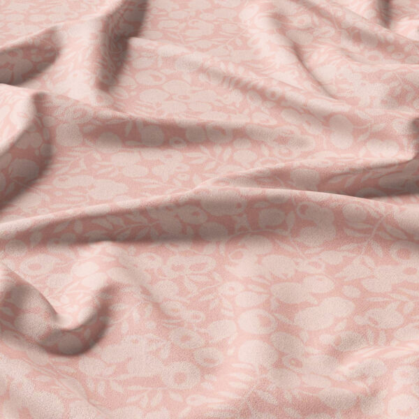 A piece of light pink fabric with a subtle floral pattern and soft, natural folds and creases.
