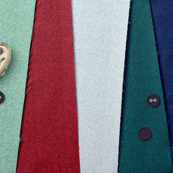 Four pieces of textured fabric in red, light blue, teal, and dark blue are arranged side by side. Three black buttons are on the fabrics, and a sewing tape measure is partially visible in the top left corner.