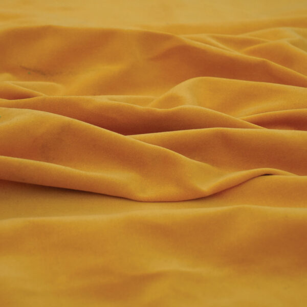A close-up view of wrinkled mustard yellow fabric with soft folds and shadows, highlighting its smooth texture.