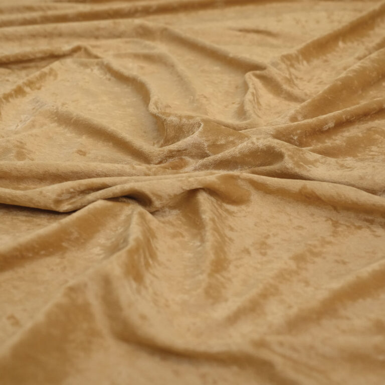 A close-up view of light brown, velvety fabric with a soft sheen, draped in gentle folds and wrinkles across a flat surface.