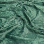 Close-up of soft, green velvet fabric with a crushed texture, showing gentle folds and a slightly shiny, reflective surface.