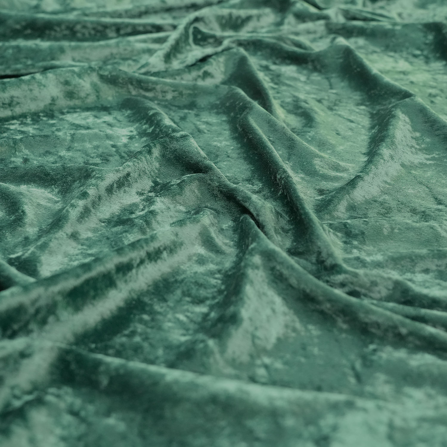 Crushed-Velvet-Forest-Green-3 Close-up of soft, green velvet fabric with a crushed texture, showing gentle folds and a slightly shiny, reflective surface.