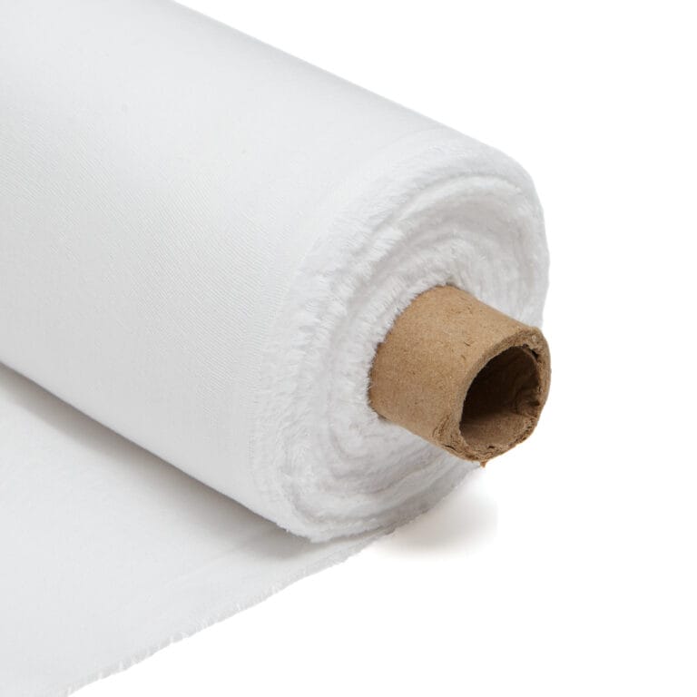 A close-up view of a roll of white fabric wrapped around a cardboard tube, with the fabric partially unrolled and laying flat on a white surface.