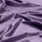 A close-up of smooth, shiny purple satin fabric with soft folds and gentle creases reflecting light.