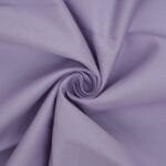 A close-up of light purple fabric twisted into a spiral, showing a smooth texture and soft folds radiating from the center.