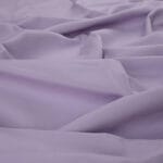 A close-up view of soft, light purple fabric with gentle folds and creases.