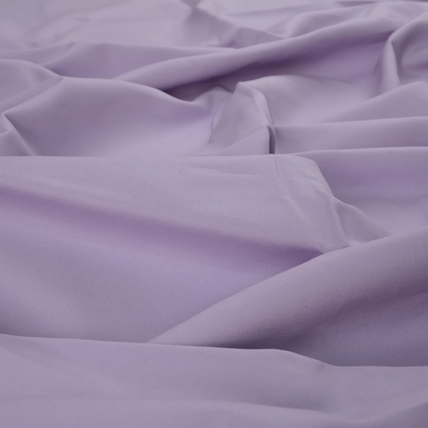 Cotton-Drill-Lilac-3 A close-up view of soft, light purple fabric with gentle folds and creases.