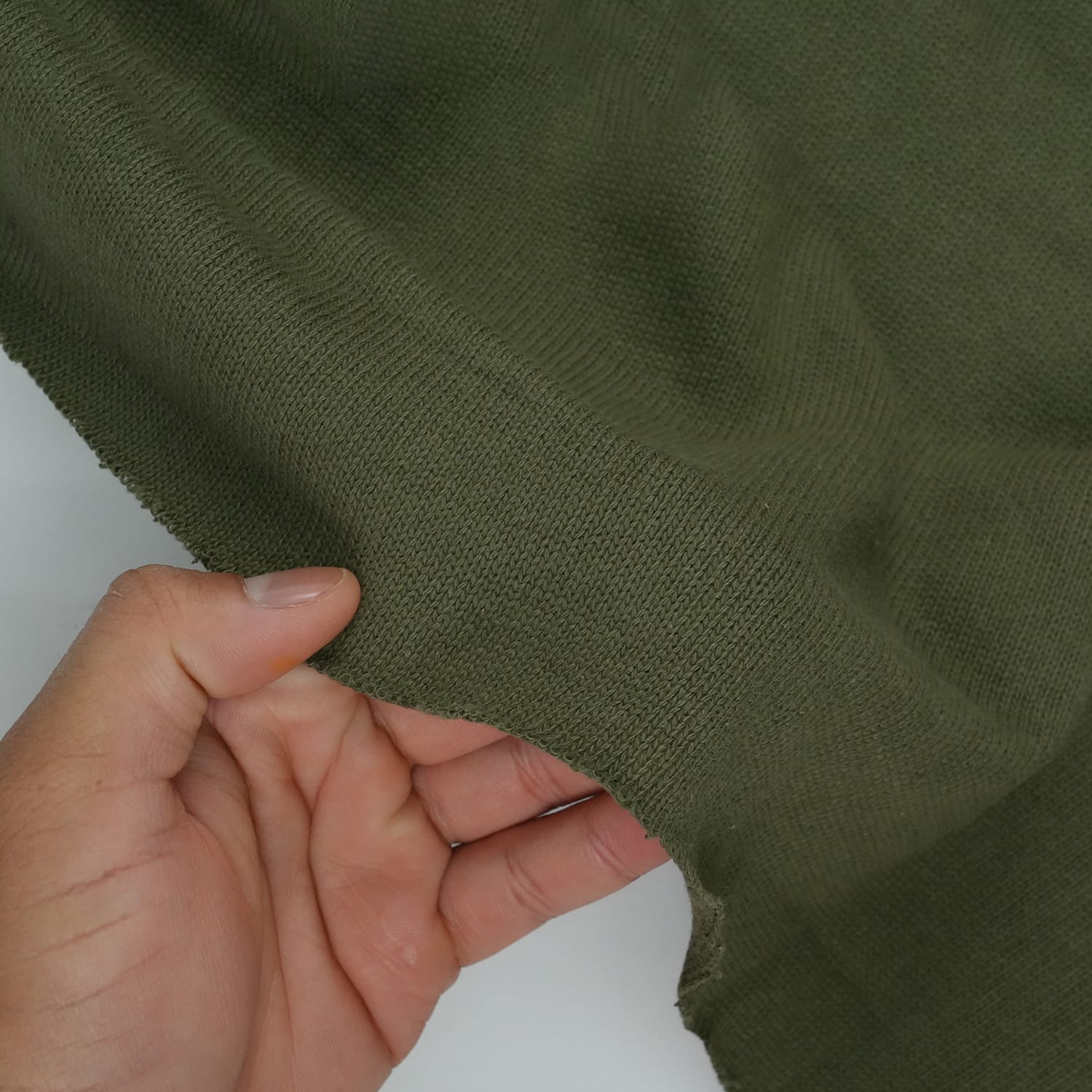 Cotton-Knitted-Prickle-5 A hand holds a piece of olive green fabric, showing its texture and stretchiness against a plain background.