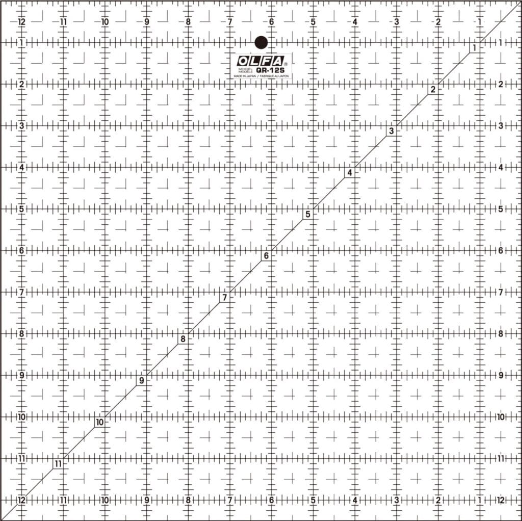 A clear OLFA QR-12S quilting ruler with black grid lines, numbers, and a diagonal line from corner to corner, marked in inches up to 12 by 12, used for measuring and cutting fabric.