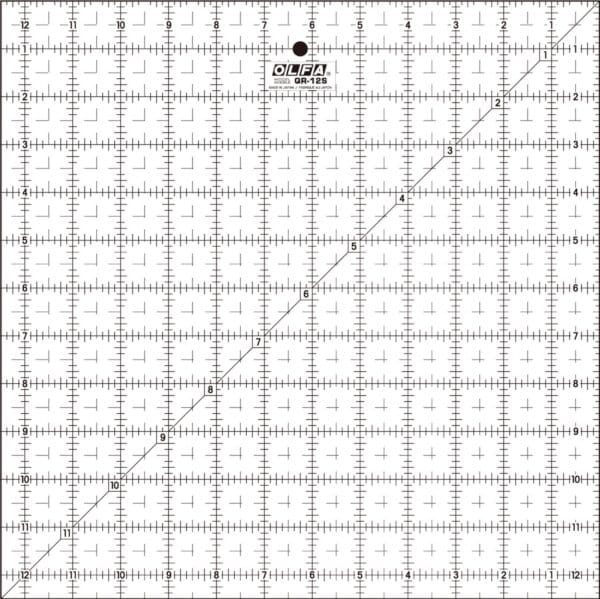 A clear OLFA QR-12S quilting ruler with black grid lines, numbers, and a diagonal line from corner to corner, marked in inches up to 12 by 12, used for measuring and cutting fabric.