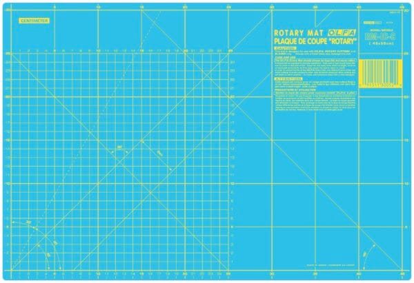 A blue OLFA rotary cutting mat with yellow gridlines, measurement markings in centimeters, diagonal lines, and printed instructions in English and French in the top right corner.