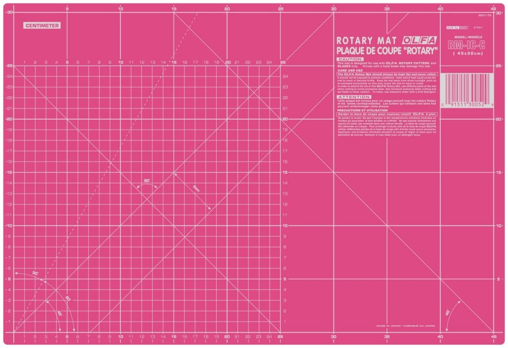 A large pink self-healing rotary cutting mat marked with a white centimeter grid, diagonal lines, angles, and measurement numbers, with product information in the top right corner.