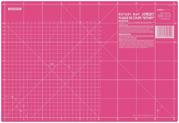 A large pink self-healing rotary cutting mat marked with a white centimeter grid, diagonal lines, angles, and measurement numbers, with product information in the top right corner.