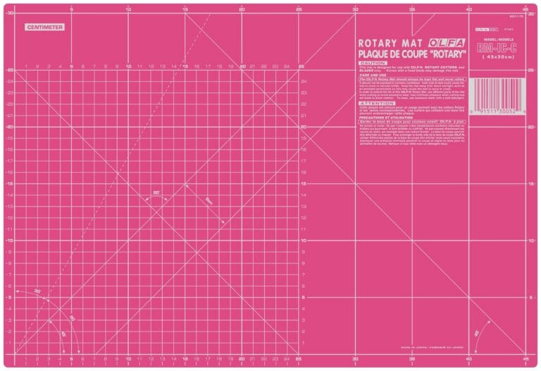 A large pink self-healing rotary cutting mat marked with a white centimeter grid, diagonal lines, angles, and measurement numbers, with product information in the top right corner.