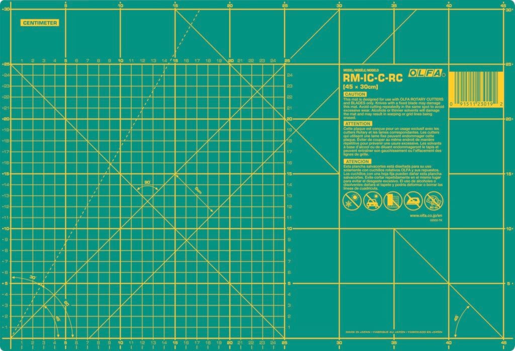A green OLFA cutting mat marked with yellow grid lines, measurement scales in centimeters, angled guides, and warning instructions, designed for precision cutting and crafting.