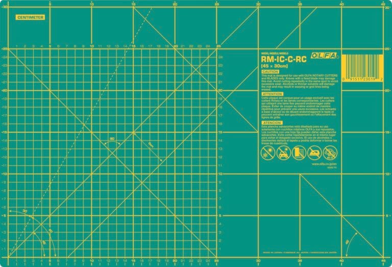 A green OLFA cutting mat marked with yellow grid lines, measurement scales in centimeters, angled guides, and warning instructions, designed for precision cutting and crafting.