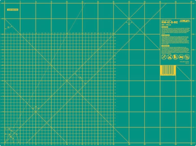 A green self-healing cutting mat with yellow grid lines, measurement marks in inches, angle guides, a barcode, safety icons, and product information in the top right corner.