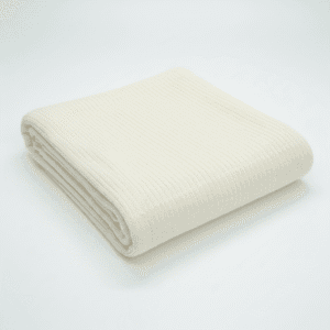 A neatly folded, cream-colored ribbed blanket is displayed on a plain white background.