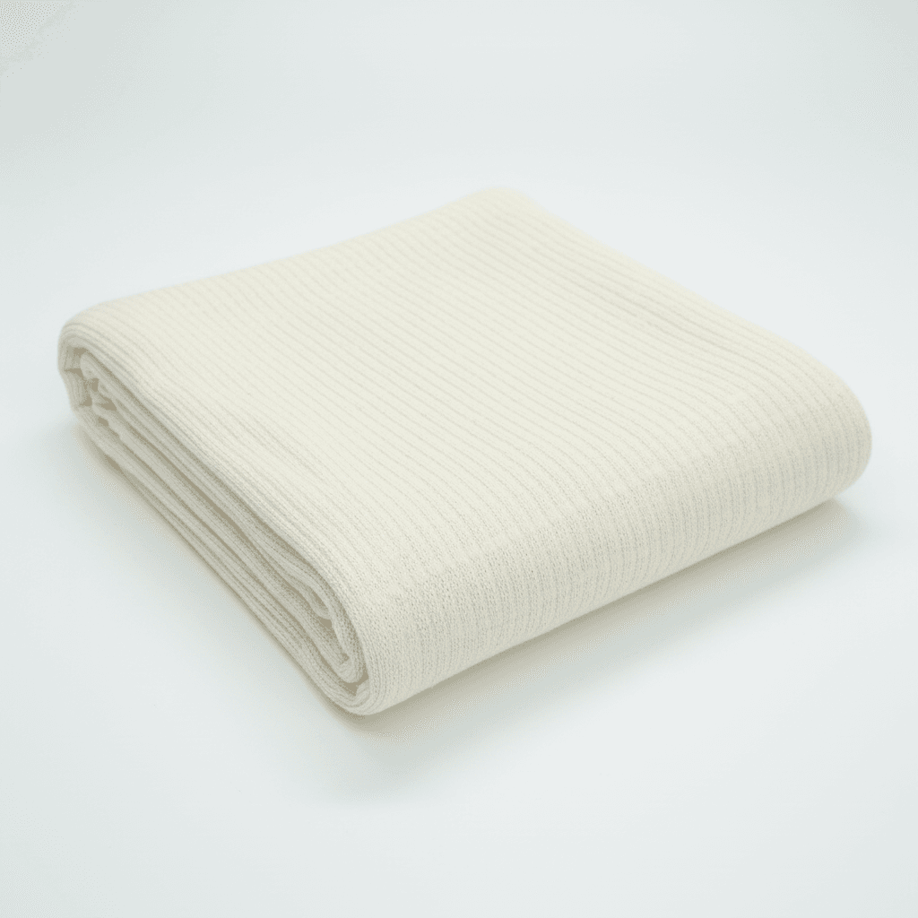 Cotton-Knitted-Cable-0 A neatly folded, cream-colored ribbed blanket is displayed on a plain white background.